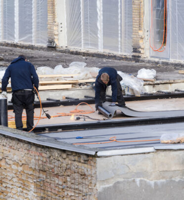 roofers installing waterproofing membrane and asphalt bitumen shingle on flat roof